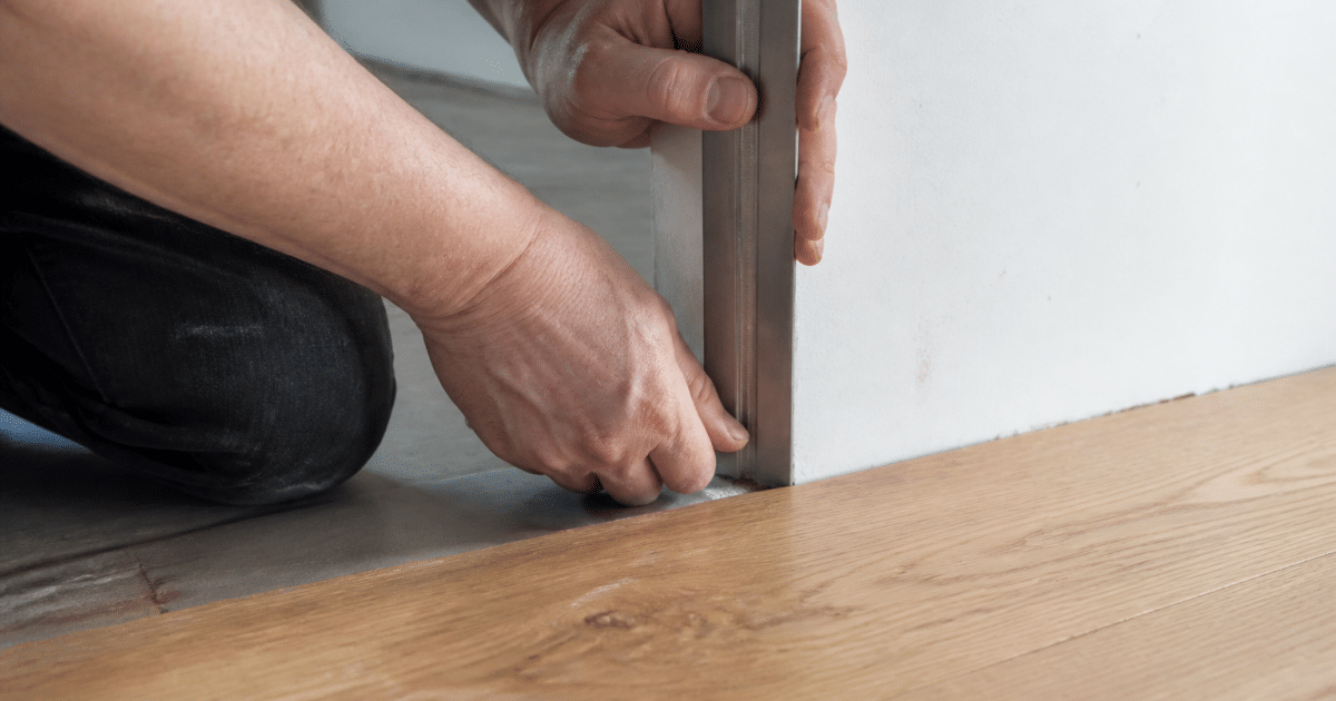 Mains appliquant profil metalique vertical contre bordure parquet bois