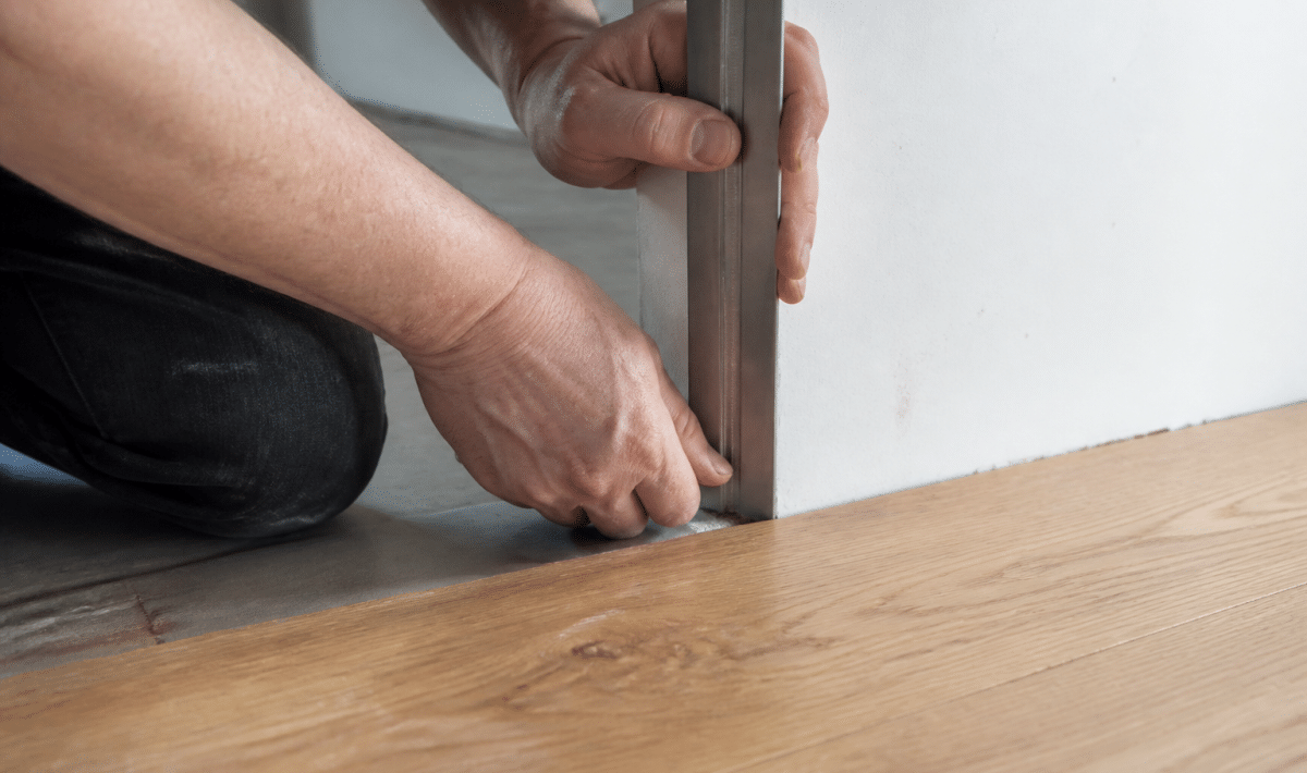 Mains appliquant profil metalique vertical contre bordure parquet bois